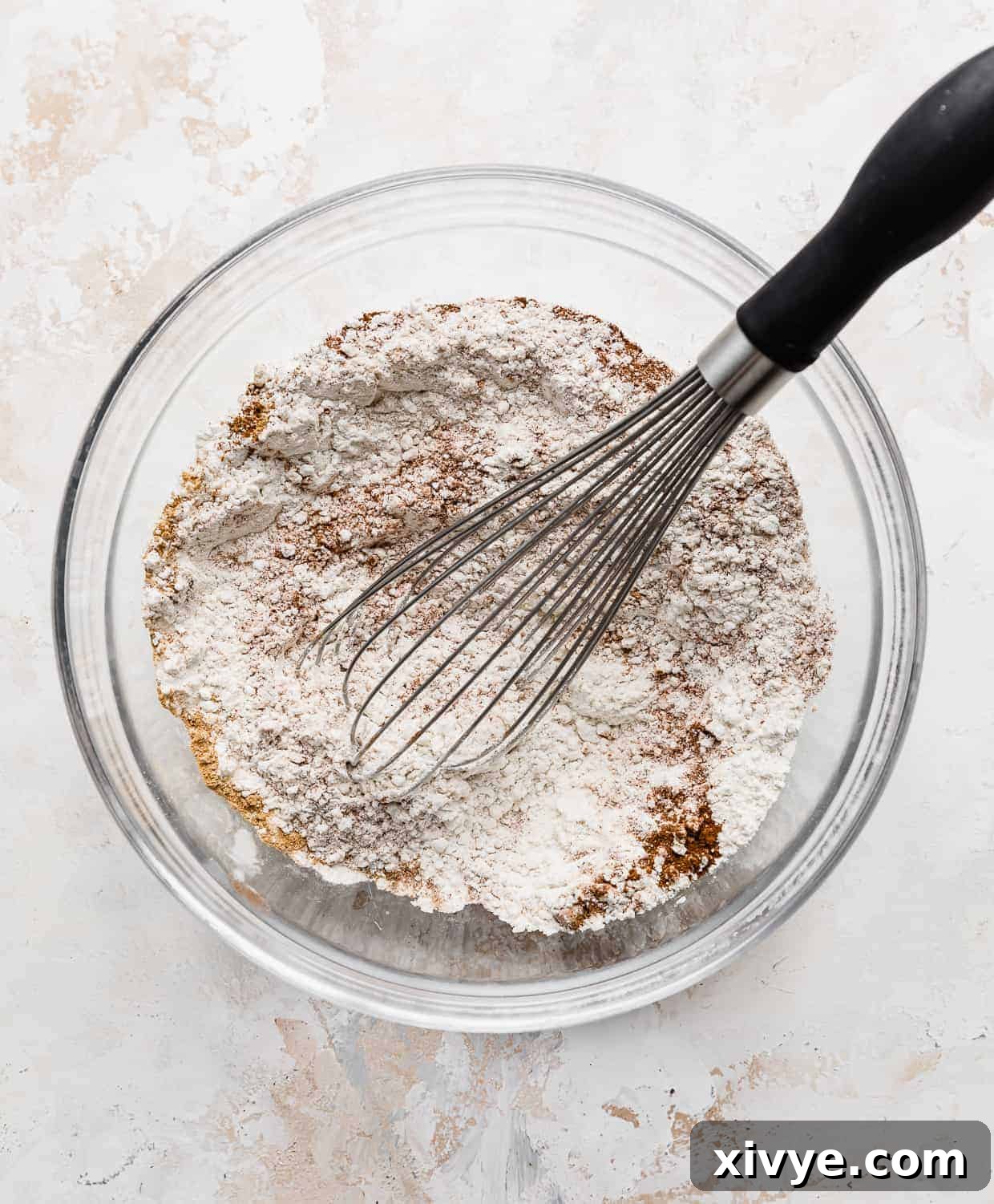 A whisk in a glass bowl, actively mixing the dry ingredients for chocolate chip pumpkin pancakes, ensuring a uniform distribution of flour, leavening agents, and aromatic spices.