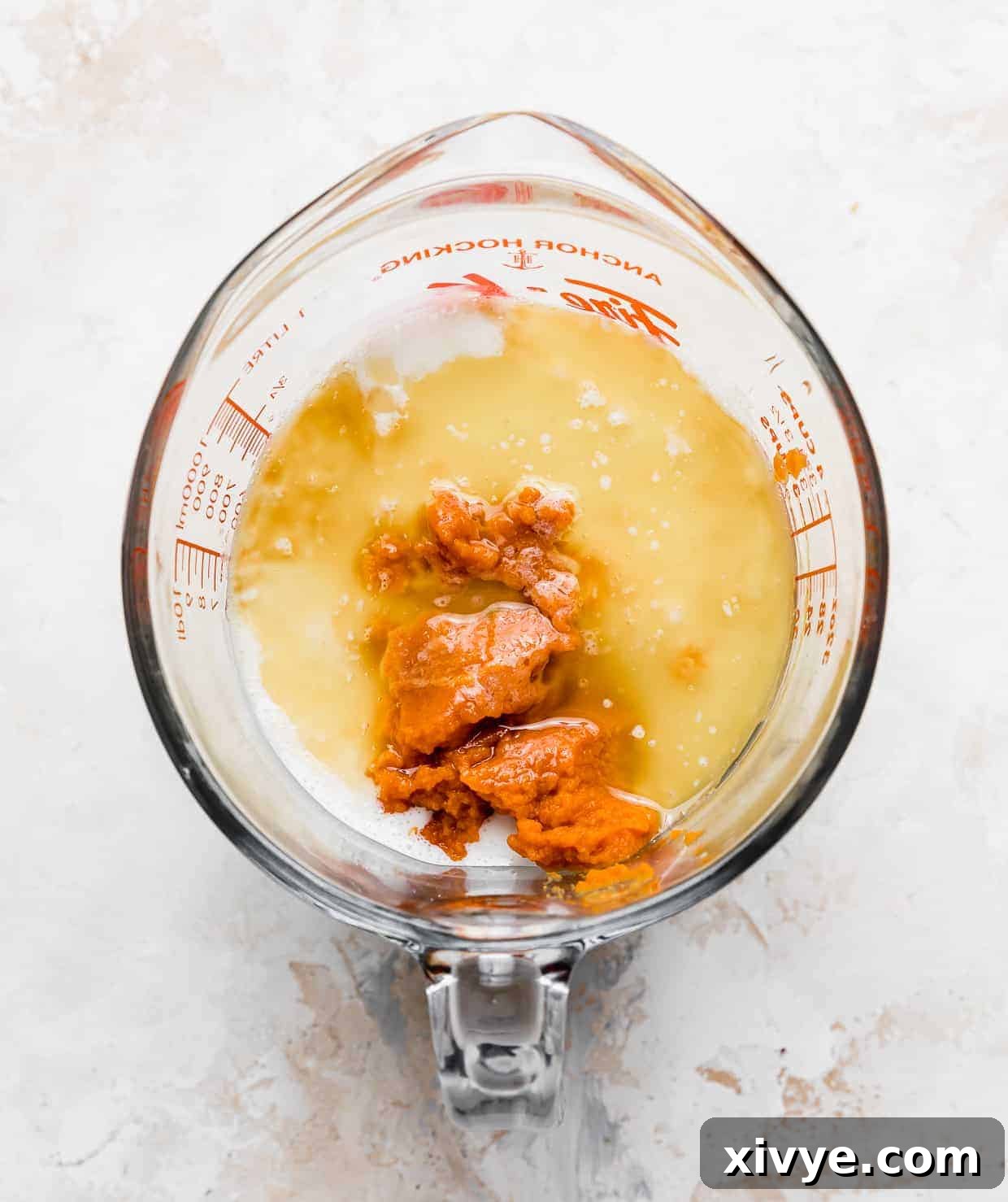 A clear glass measuring cup containing a beautiful blend of pumpkin puree, rich melted butter, and creamy buttermilk, prepared for the wet ingredients of the pancake batter.