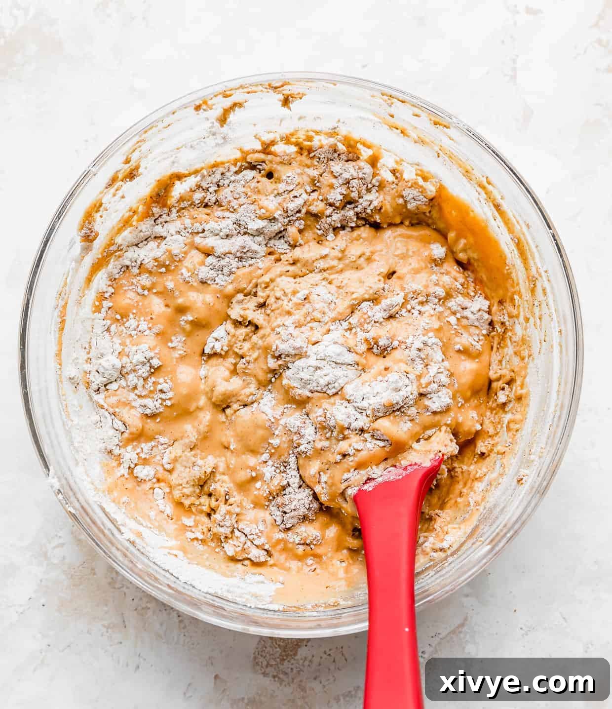 A spatula gently stirring the vibrant orange pumpkin chocolate chip pancake batter in a glass bowl, illustrating the minimal mixing required for a light and fluffy result.