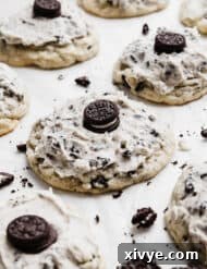 A close-up shot of a Crumbl Cookies and Cream Milkshake Cookie resting on white parchment paper, highlighting its frosted top and mini Oreo garnish.