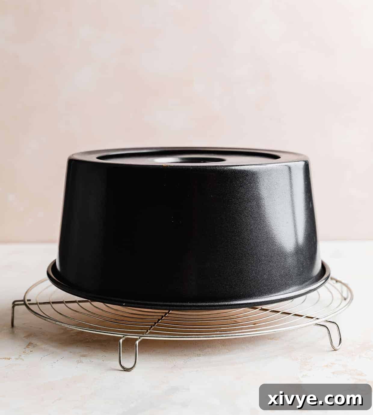 An inverted tube pan containing a freshly baked angel food cake, resting on a circular wire cooling rack.