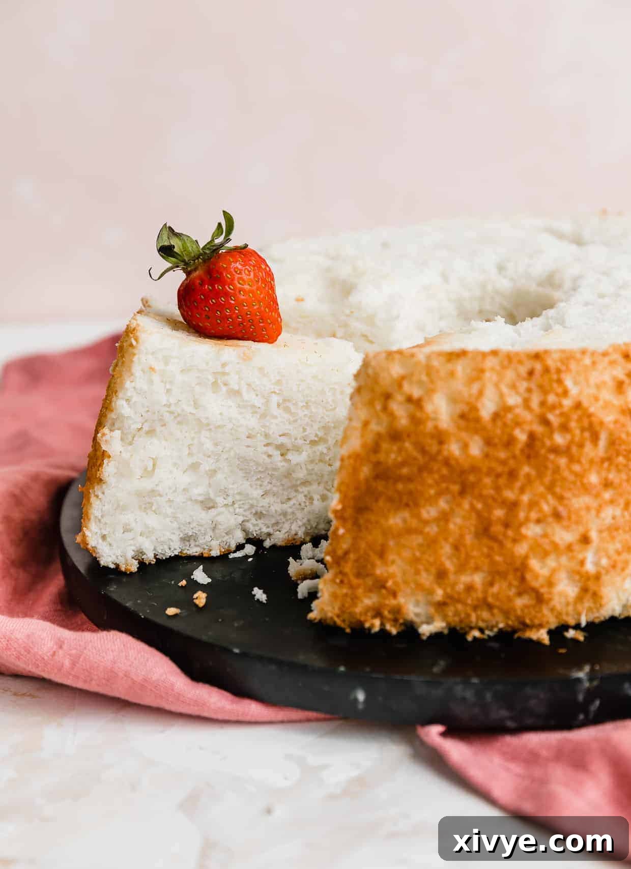 A beautifully baked homemade angel food cake displayed on a sleek black plate, showcasing its golden crust and delicate form.