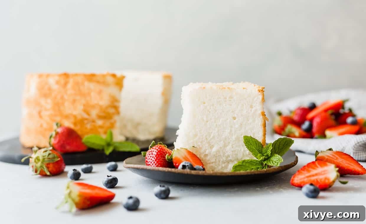 A perfect slice of angel food cake artfully arranged on a plate, surrounded by a delightful scattering of fresh strawberries and blueberries.