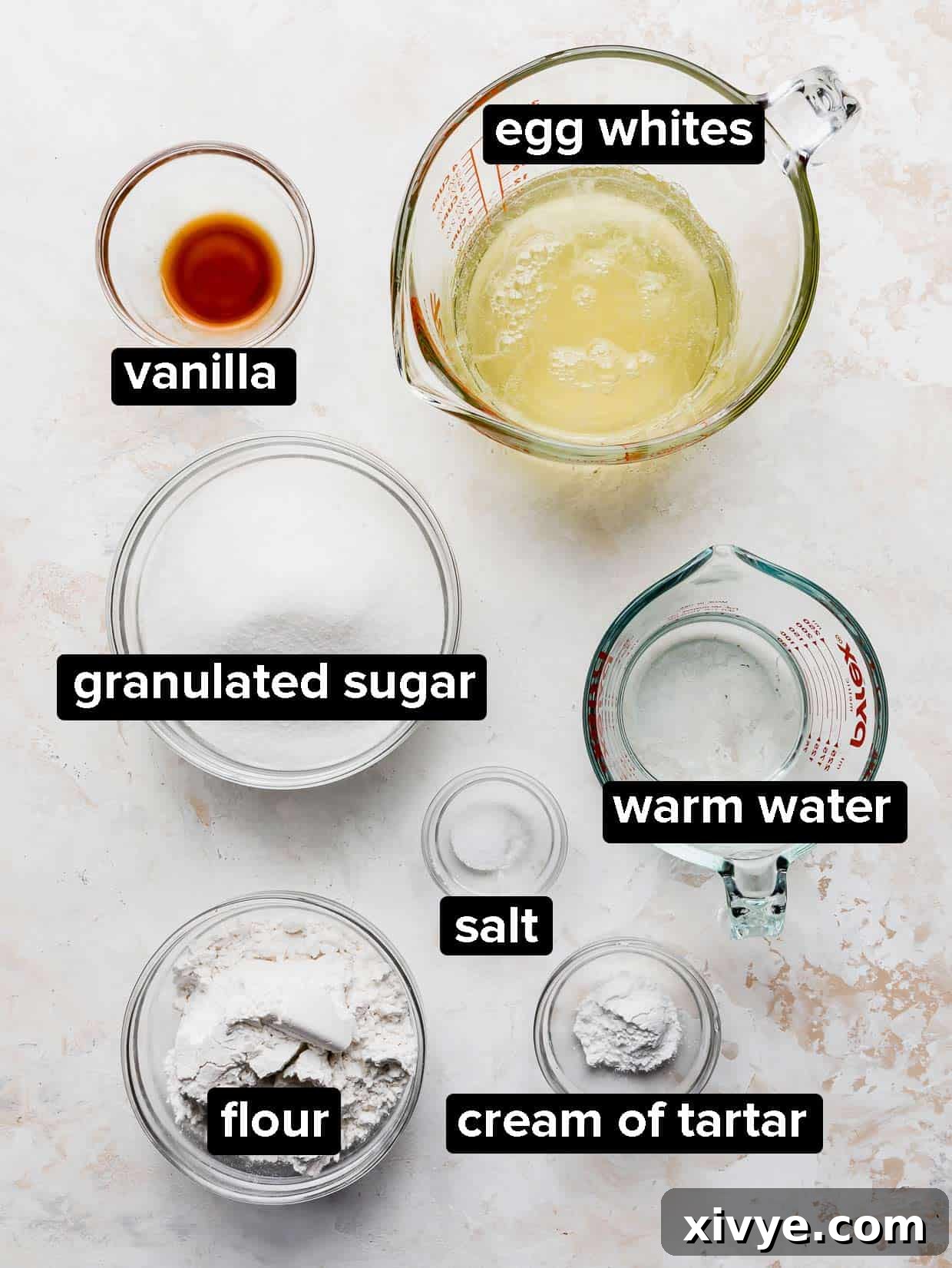 A curated collection of ingredients required for baking a classic angel food cake, artfully arranged on a subtly textured cream background.