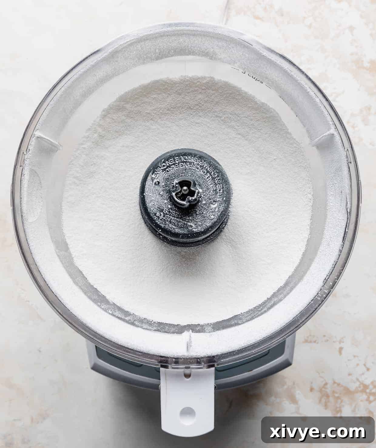 A food processor containing a generous amount of granulated sugar, ready for processing.
