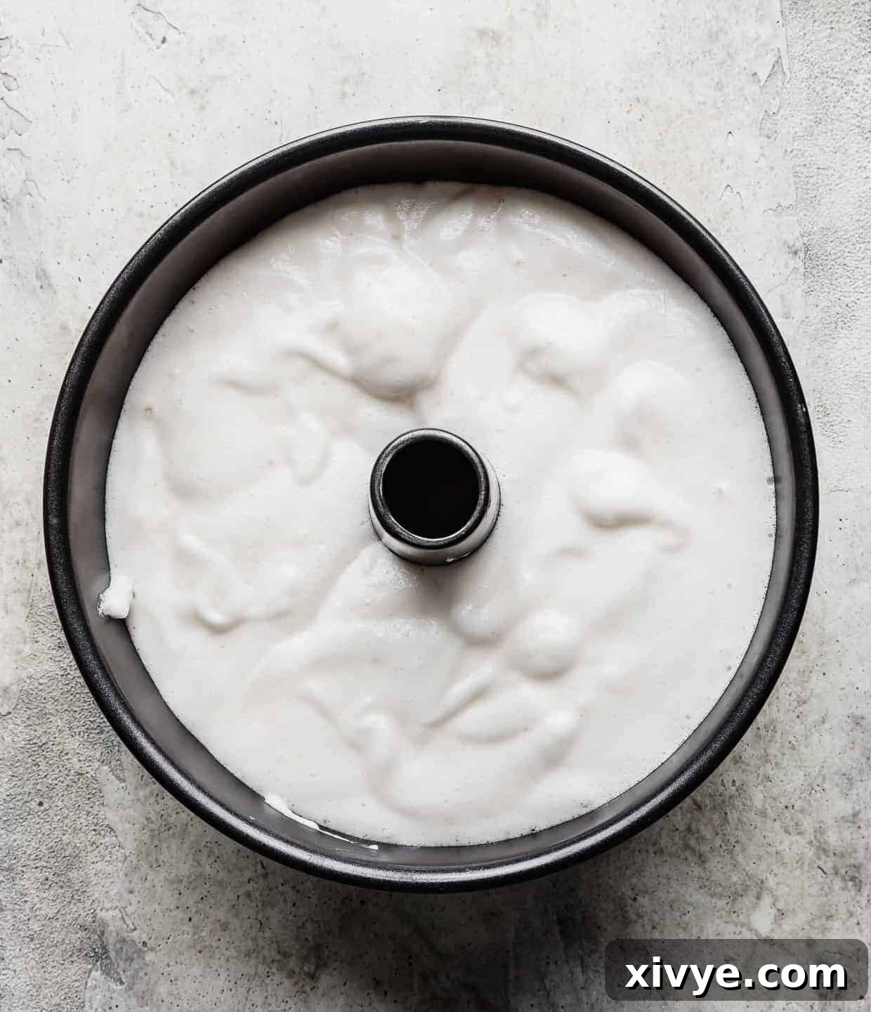 Delicate angel food cake batter meticulously scooped into an ungreased tube pan, ready for baking.