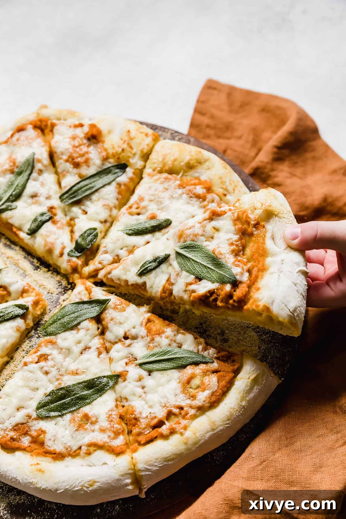 A hand pulling a slice of Pumpkin Pizza from the large pizza.
