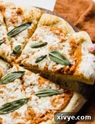 A small hand holding up a slice of Pumpkin Pizza.