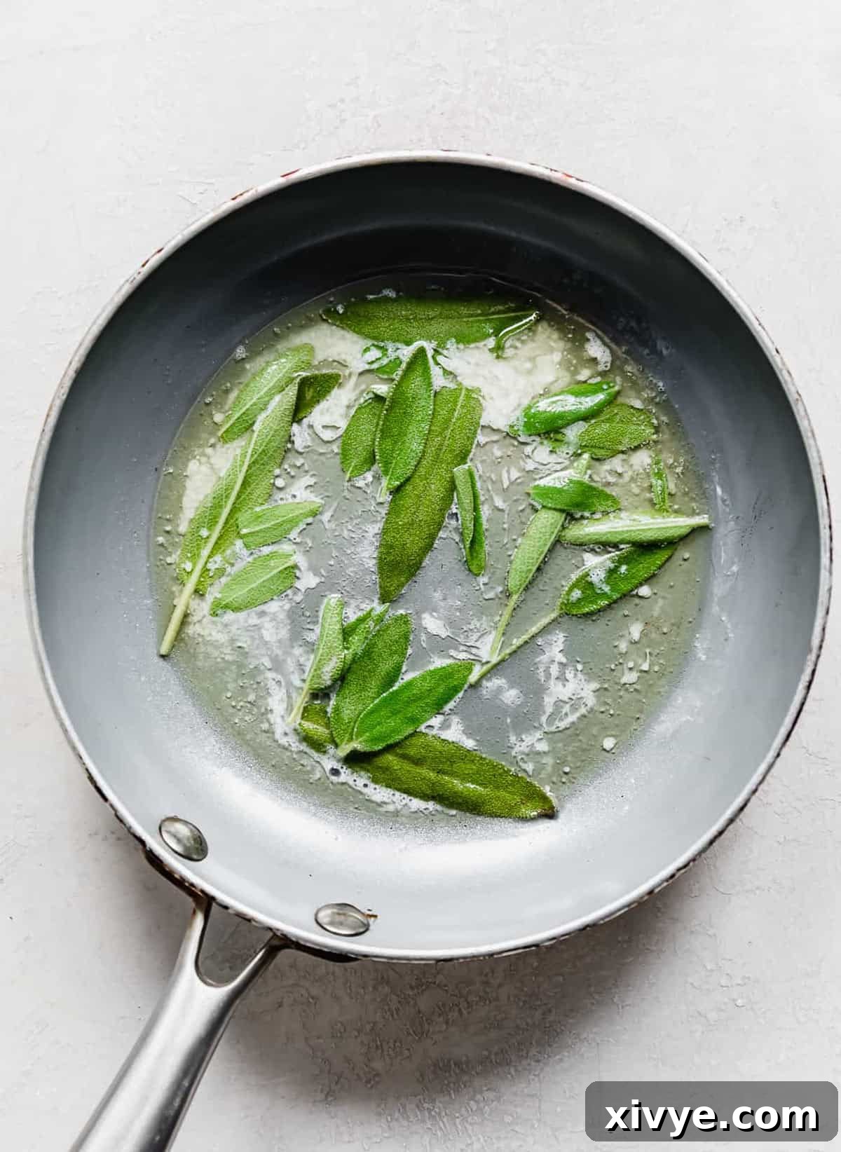 A gray skillet with melted butter and fresh sage leaves in it.