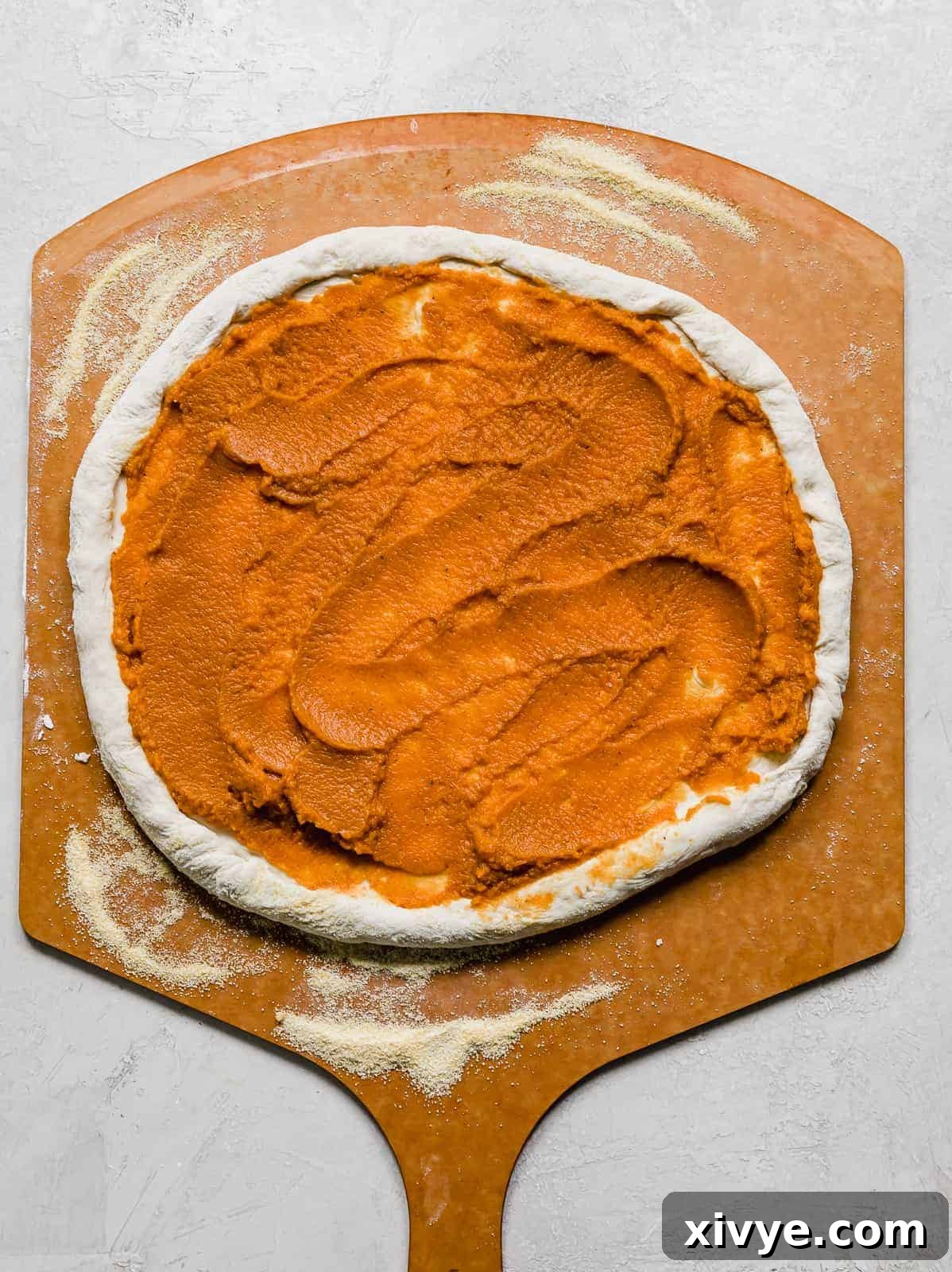 A pumpkin puree topped pizza dough on a pizza peel.