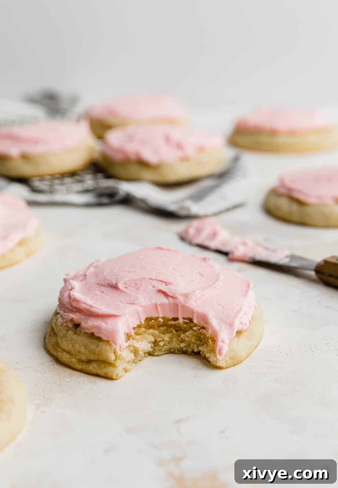 Perfect Crumbl Pink Sugar Cookie Recipe 2 A soft, round sugar cookie topped with a generous swirl of pink almond frosting, presented on a clean white background.