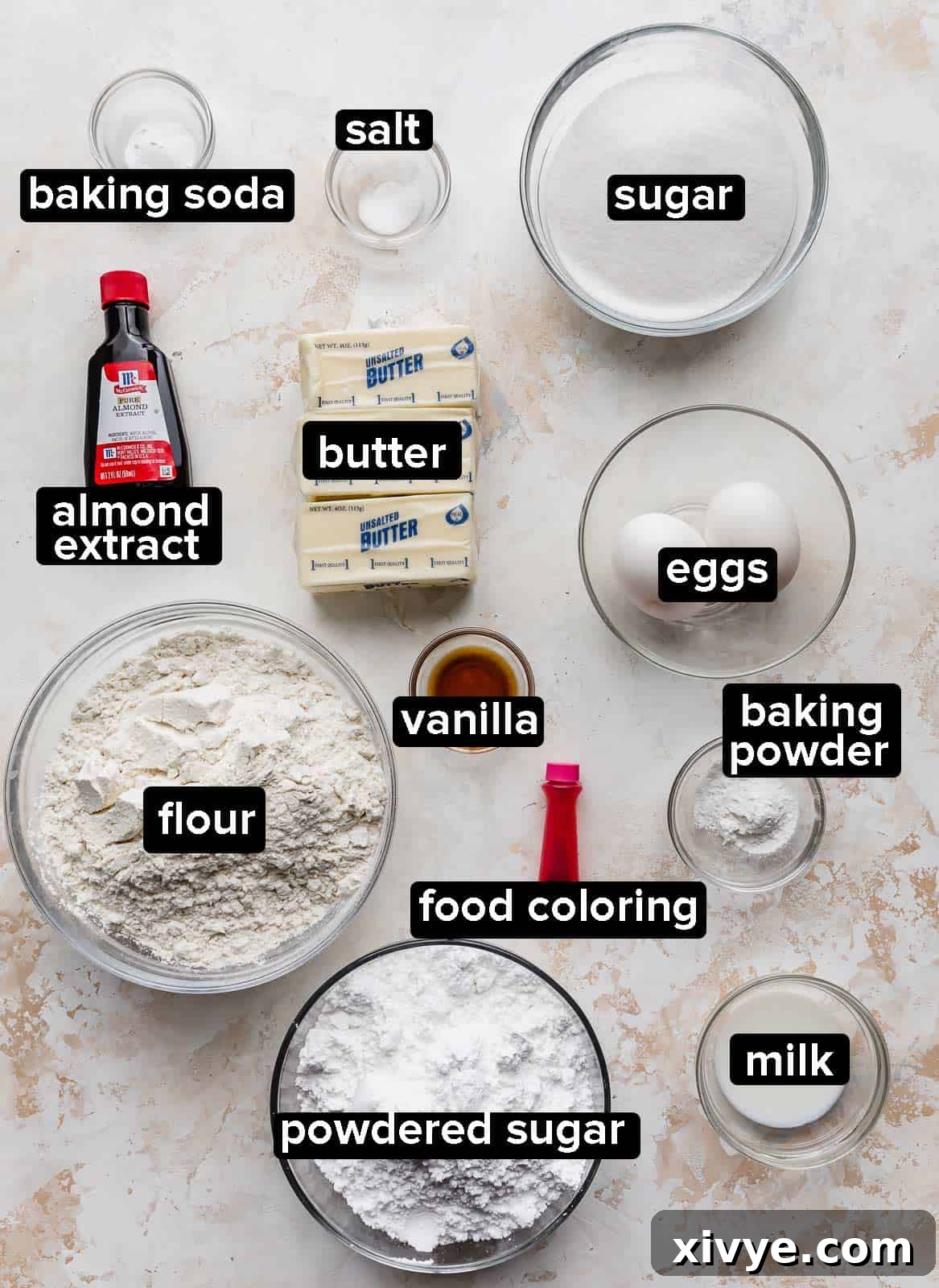 Perfect Crumbl Pink Sugar Cookie Recipe 4 Various baking ingredients neatly arranged on a rustic gray background, including flour, sugar, butter, and extracts, ready for making copycat Crumbl sugar cookies.