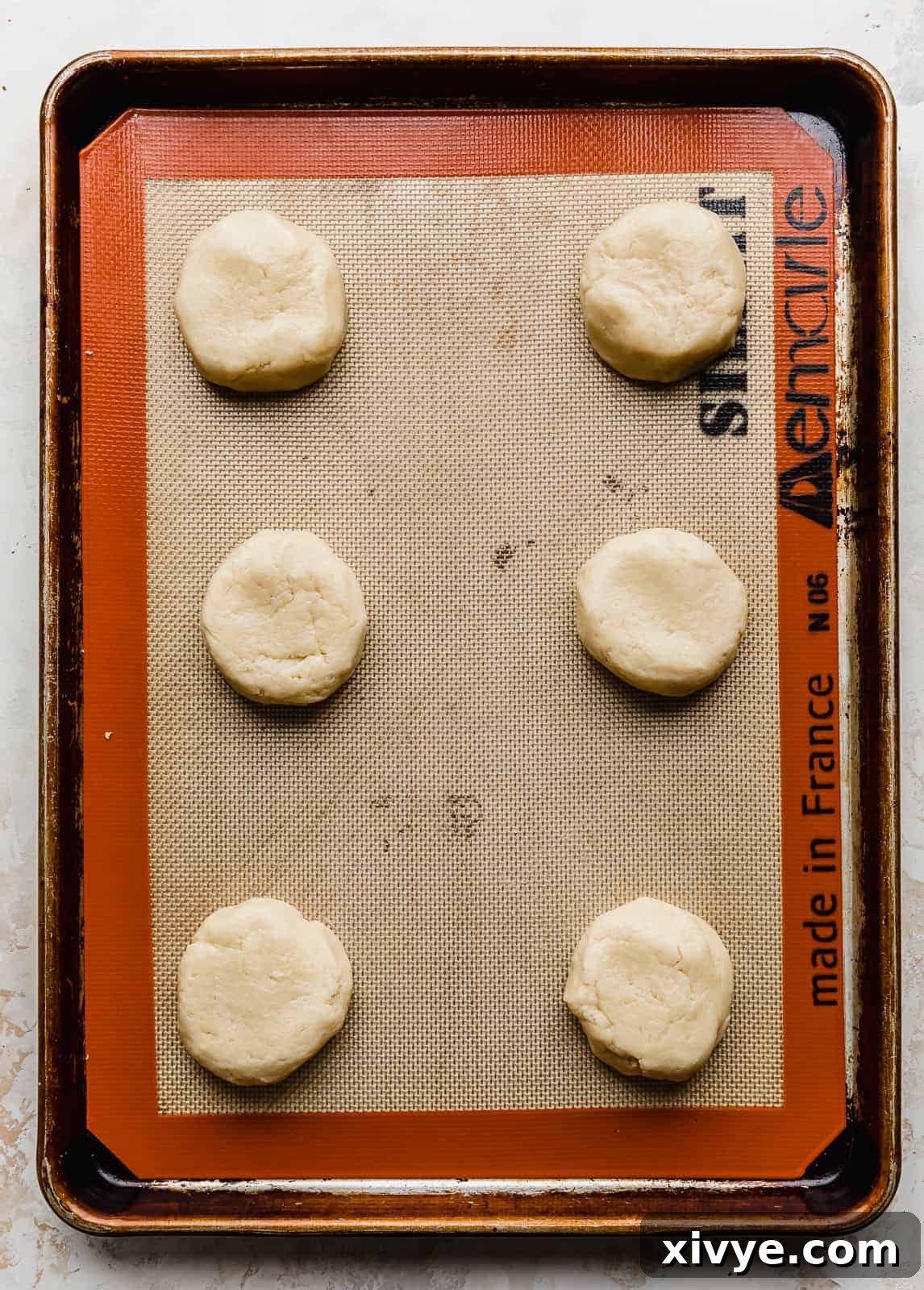 Perfect Crumbl Pink Sugar Cookie Recipe 6 Six perfectly portioned sugar cookie dough balls flattened into discs on a parchment-lined baking sheet, ready for the oven.