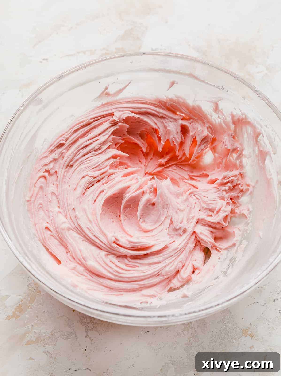 Perfect Crumbl Pink Sugar Cookie Recipe 8 Rich, vibrant pink almond frosting swirled in a clear glass bowl, ready to be spread onto copycat Crumbl sugar cookies.