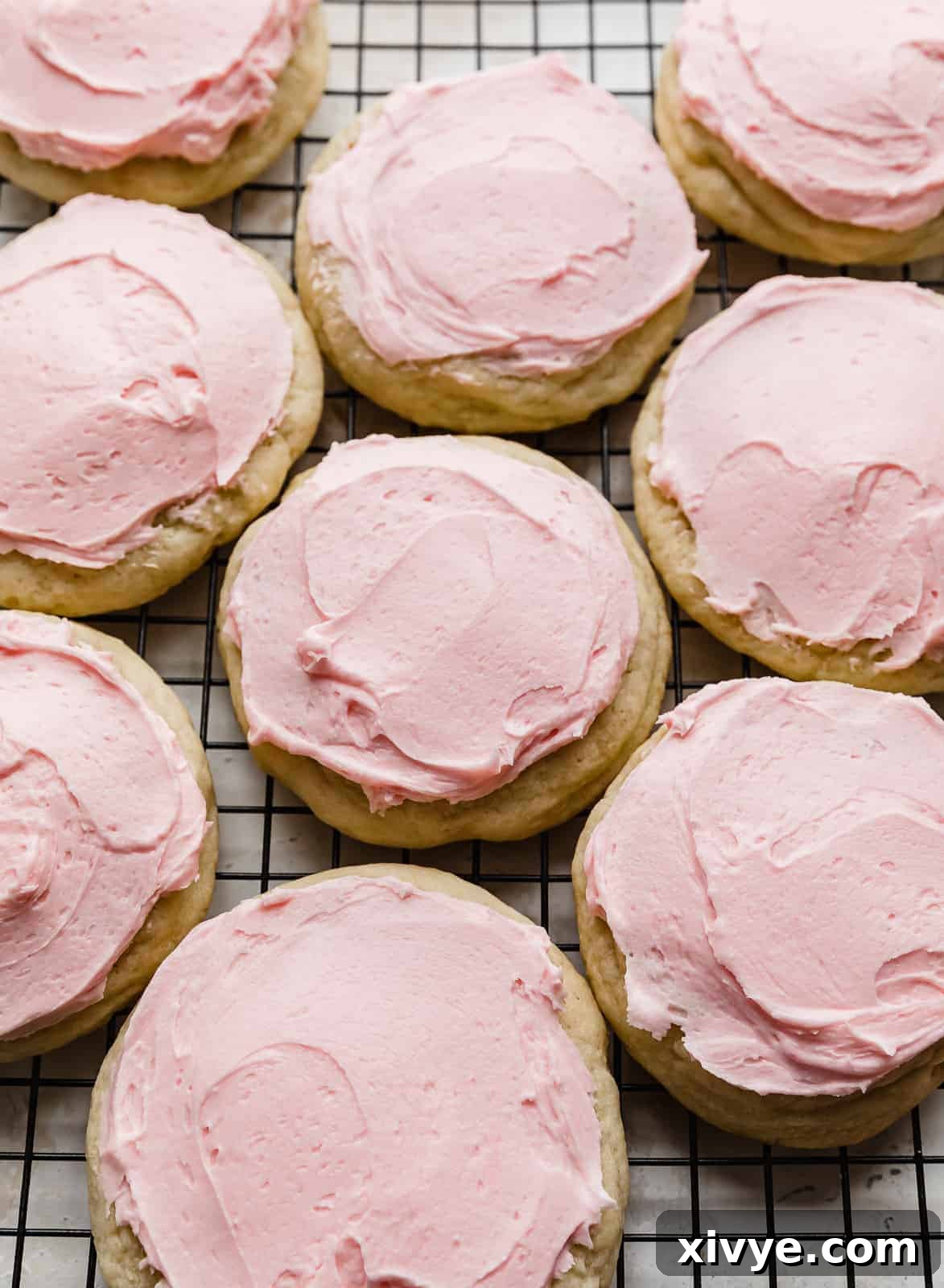 Perfect Crumbl Pink Sugar Cookie Recipe 9 A selection of freshly frosted copycat Crumbl Sugar Cookies on a black wire cooling rack, ready to be enjoyed or chilled.