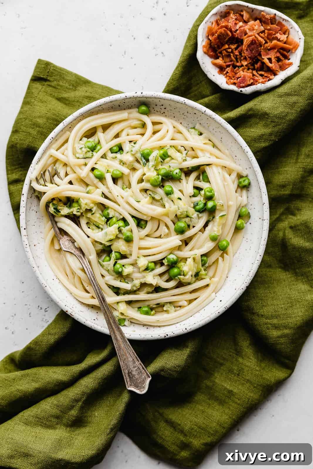 Creamy Zucchini Pasta 2 A white plate with Pasta with Zucchini Sauce and vibrant green peas, garnished with fresh herbs.