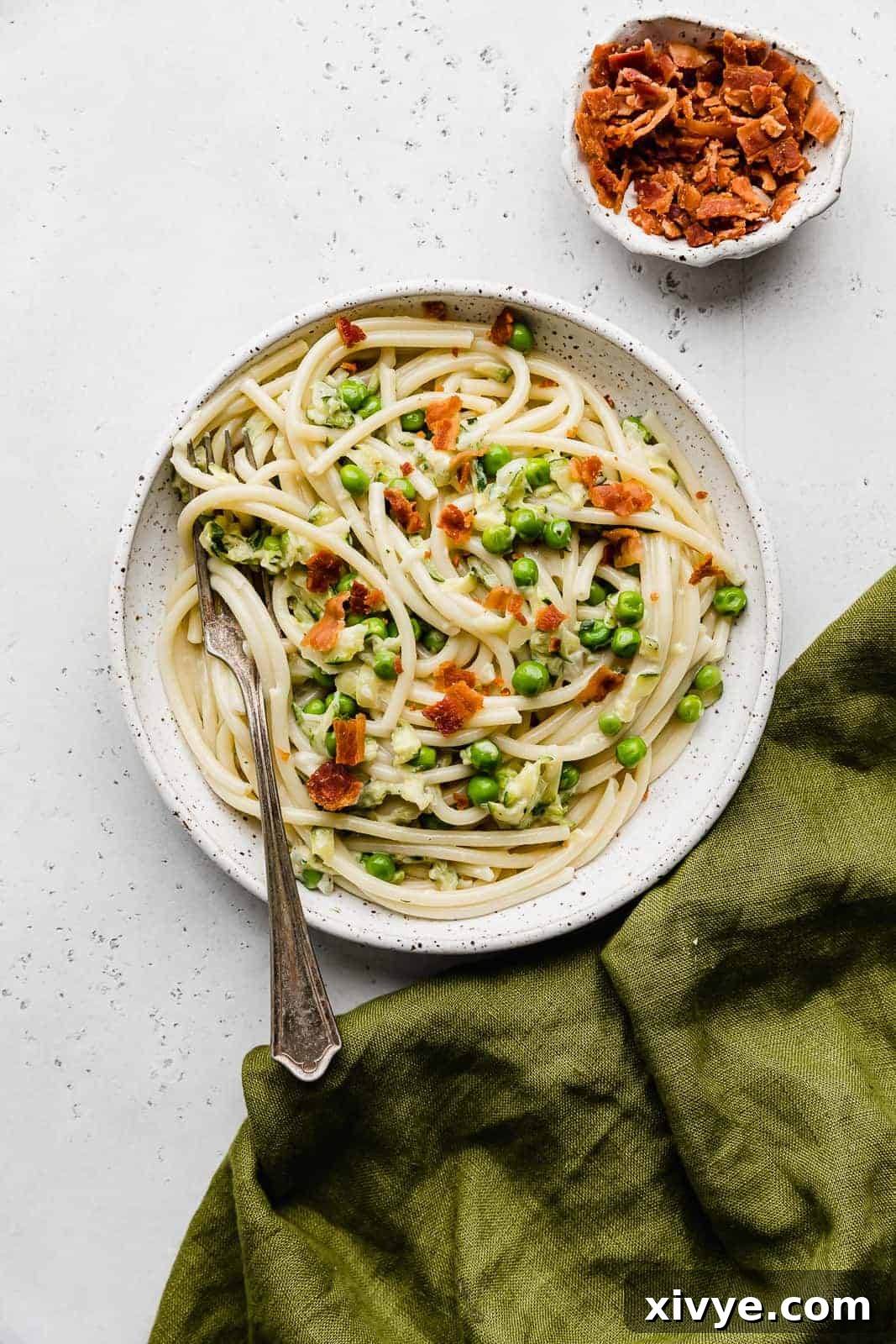 Creamy Zucchini Pasta 12 A white plate featuring Bacon Pasta with Zucchini Sauce, garnished with fresh herbs.