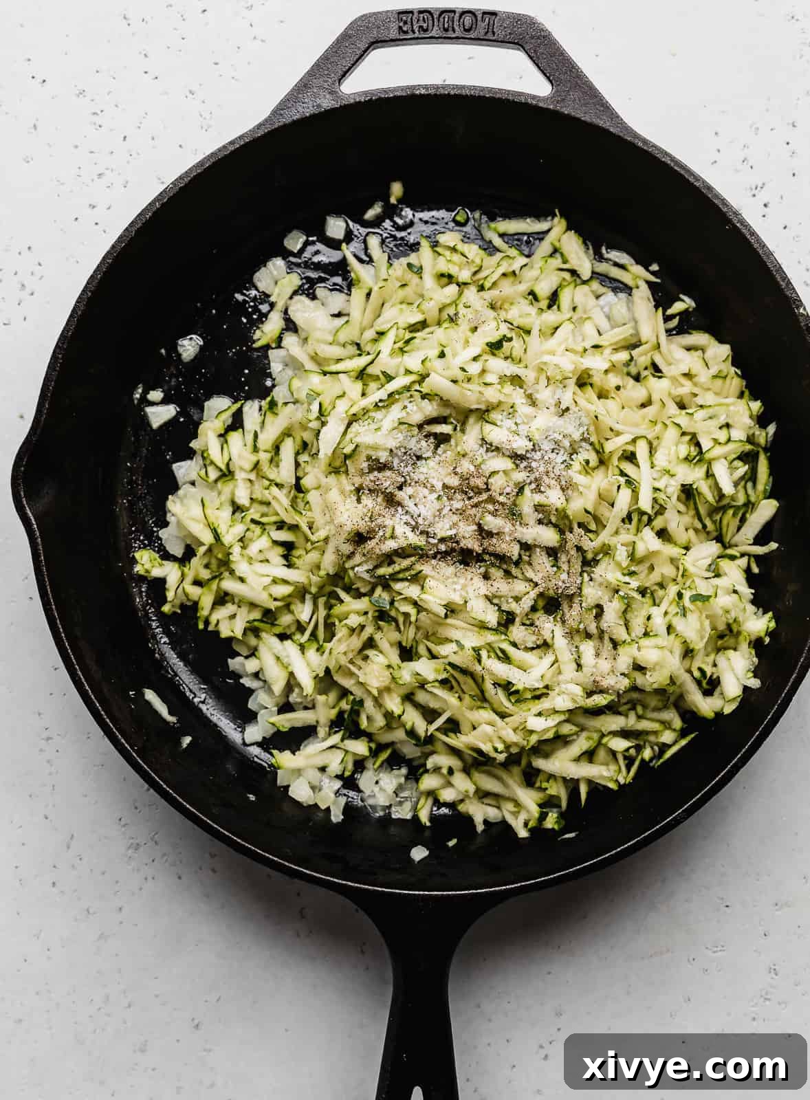 Creamy Zucchini Pasta 4 A black skillet containing freshly shredded zucchini sautéing over medium heat.