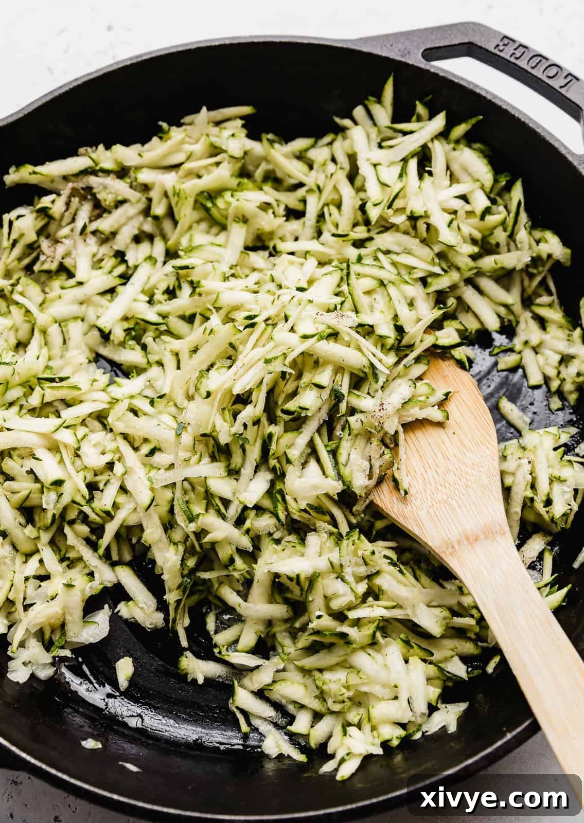 Creamy Zucchini Pasta 5 A close-up photograph showcasing the texture of shredded zucchini as it cooks down in a black skillet.
