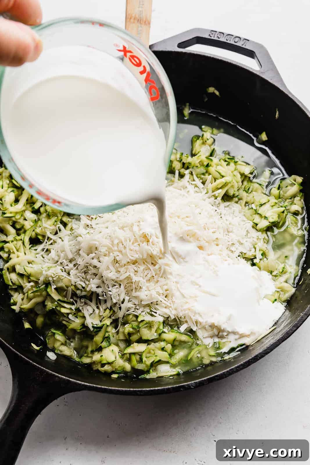 Creamy Zucchini Pasta 7 Heavy cream being gracefully poured over sautéed shredded zucchini in a black skillet, beginning the creamy sauce creation.