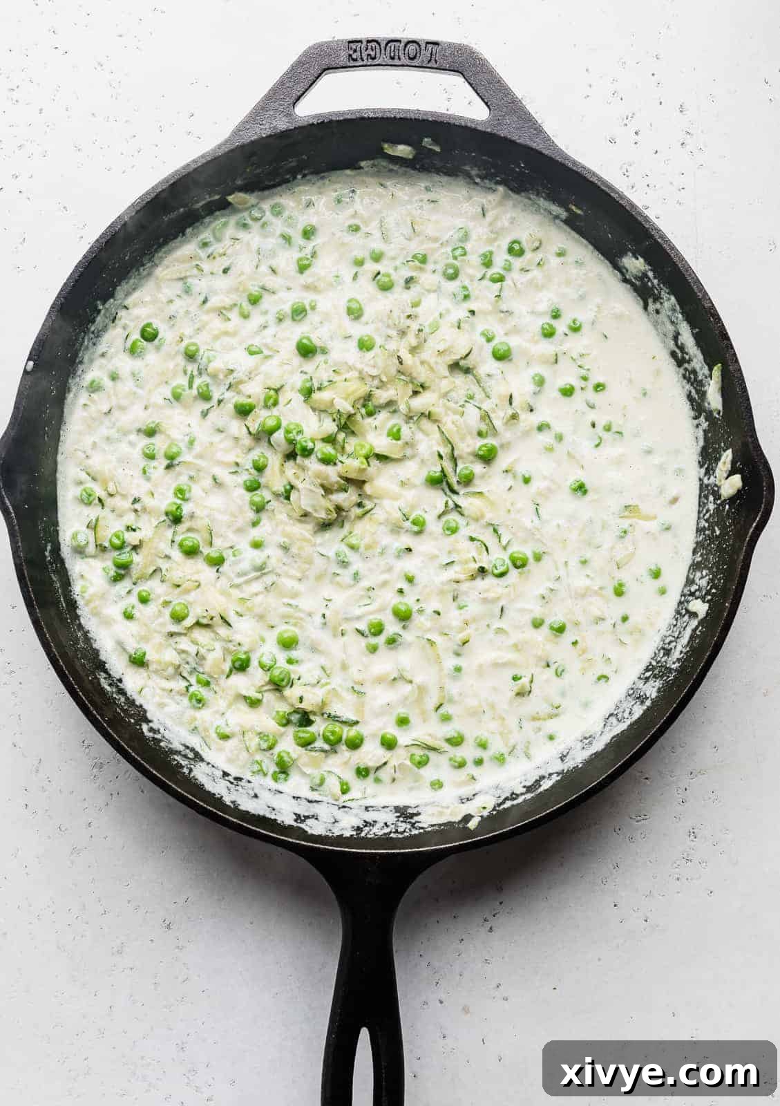 Creamy Zucchini Pasta 9 A close-up view of a black skillet featuring shredded zucchini fully incorporated into a creamy white sauce.