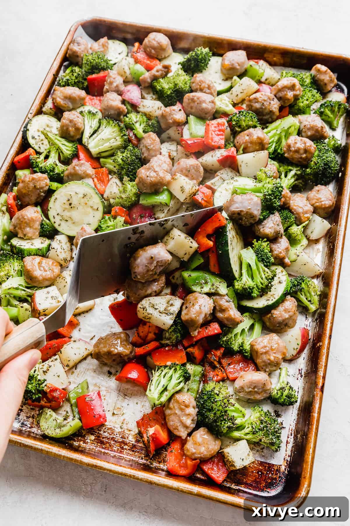One-Pan Italian Sausage and Roasted Vegetables 8 A metal spatula turning over sausage and veggies on a sheet pan.