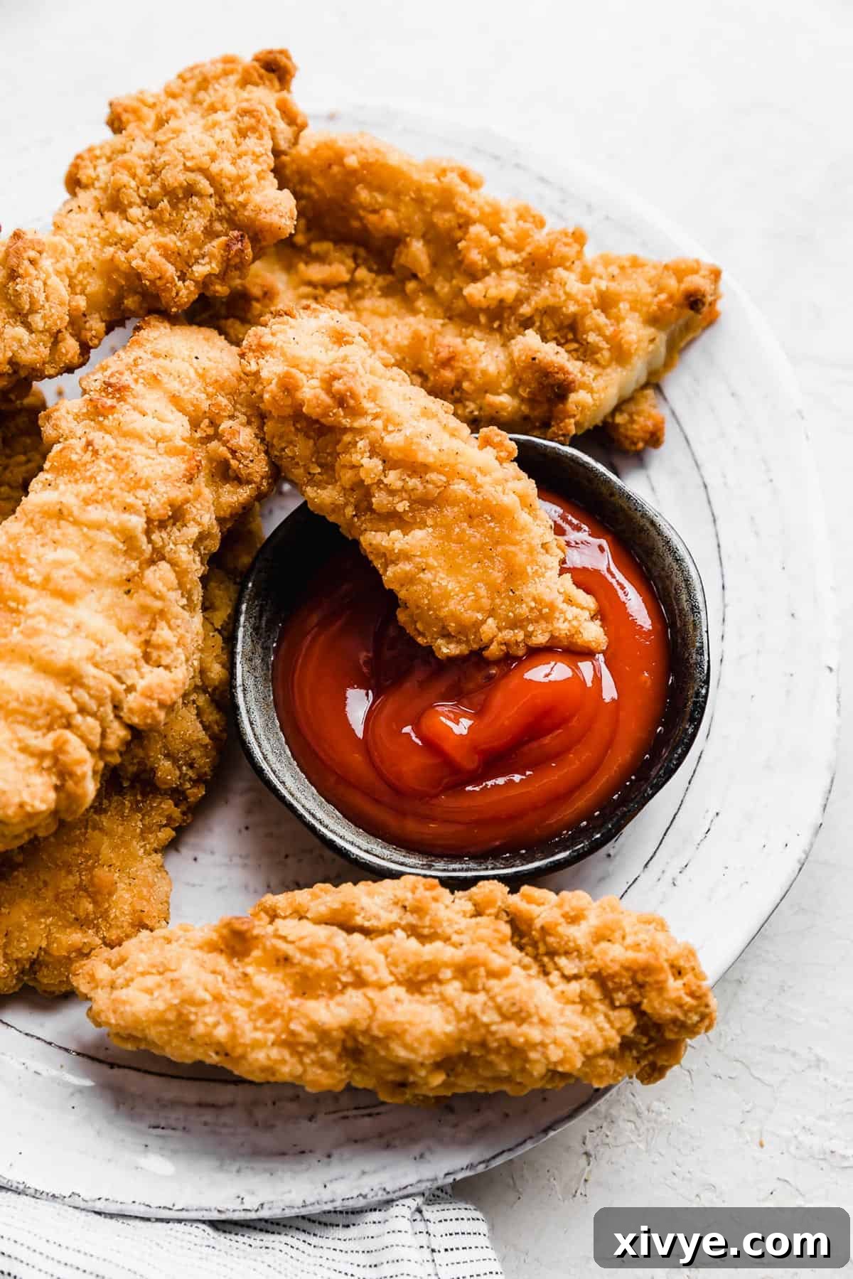 A golden chicken tender, cooked to perfection in the air fryer, dipping into a small bowl of vibrant red ketchup.