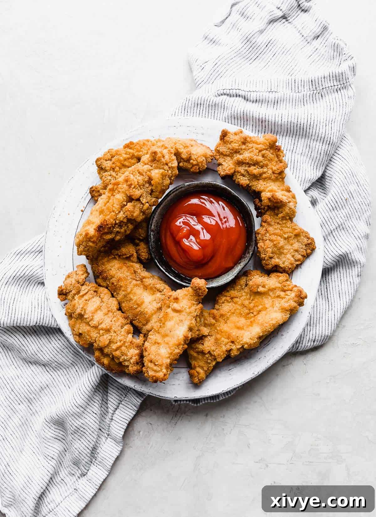 Perfectly cooked Air Fryer Frozen Chicken Tenders arranged on a clean white plate against a minimalist white background.