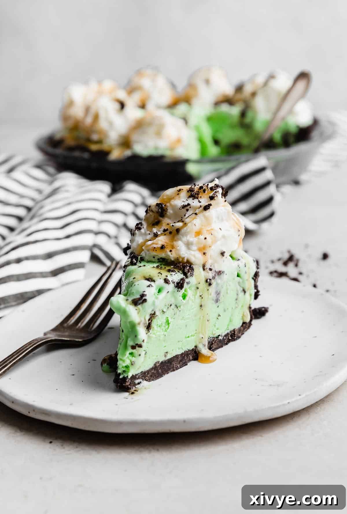 Concrete Crumble 10 A delicious slice of Asphalt Pie on a white plate, showcasing its layered beauty with whipped cream, caramel, and crushed Oreos.