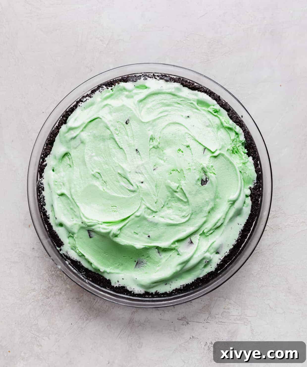 Concrete Crumble 4 A deep dish Oreo crust filled with a perfectly smooth layer of vibrant green mint chocolate chip ice cream, ready for freezing.