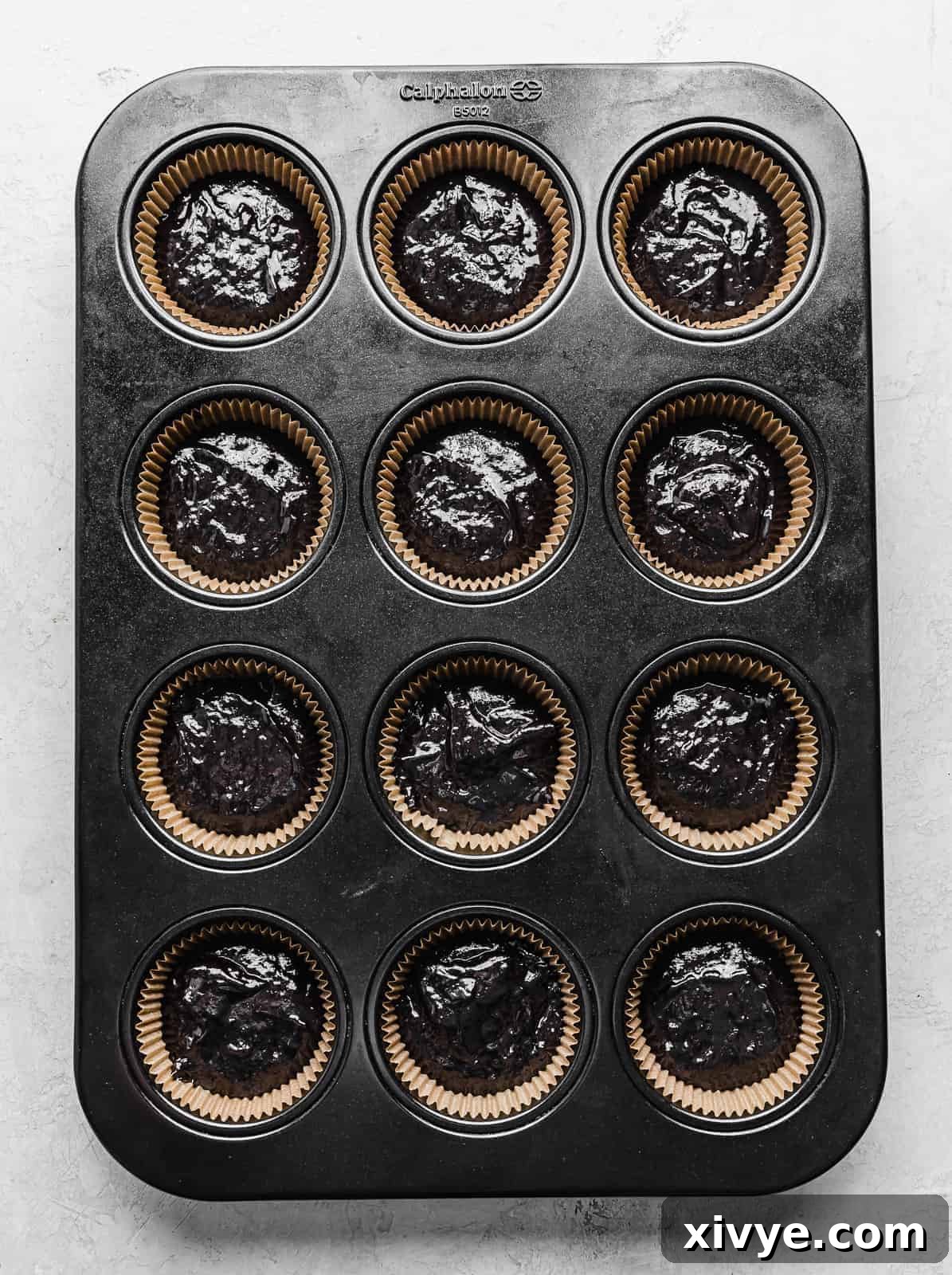 A cupcake pan with Black Velvet Cupcake batter meticulously portioned into each paper-lined compartment, ready for baking.
