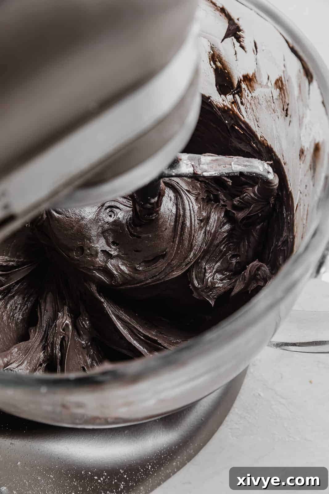 A stand mixer actively stirring the ingredients for Black Velvet Cupcake frosting, illustrating the whipping process to achieve a smooth consistency.