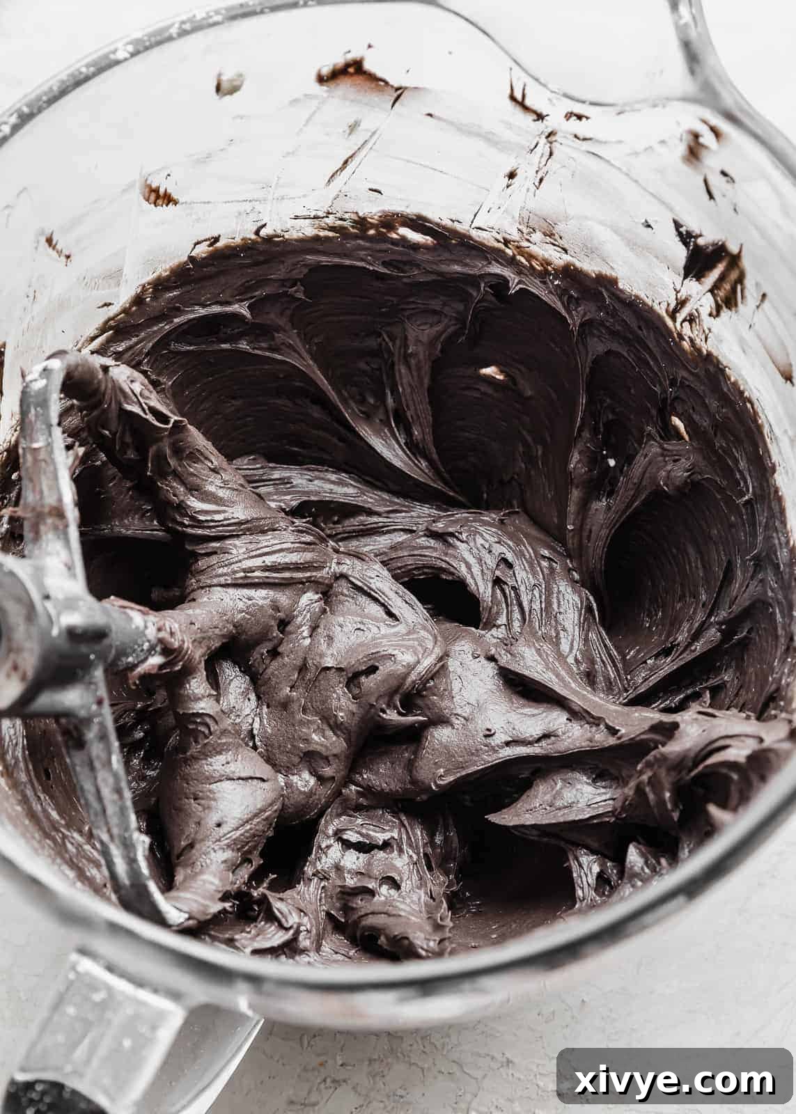 A smooth, dark black cream cheese frosting for Black Velvet Cupcakes, perfectly whipped and resting in a clear glass bowl, ready for piping.