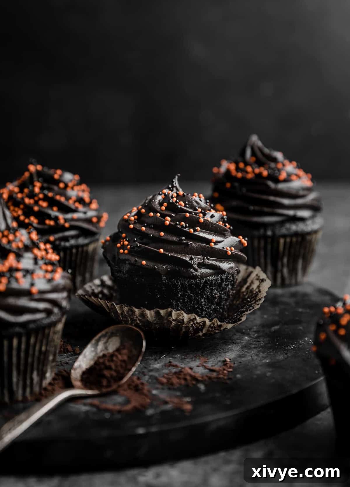 Beautifully frosted Black Velvet Cupcakes adorned with vibrant orange sprinkles, arranged on a black plate against a dark background, perfect for a spooky celebration.