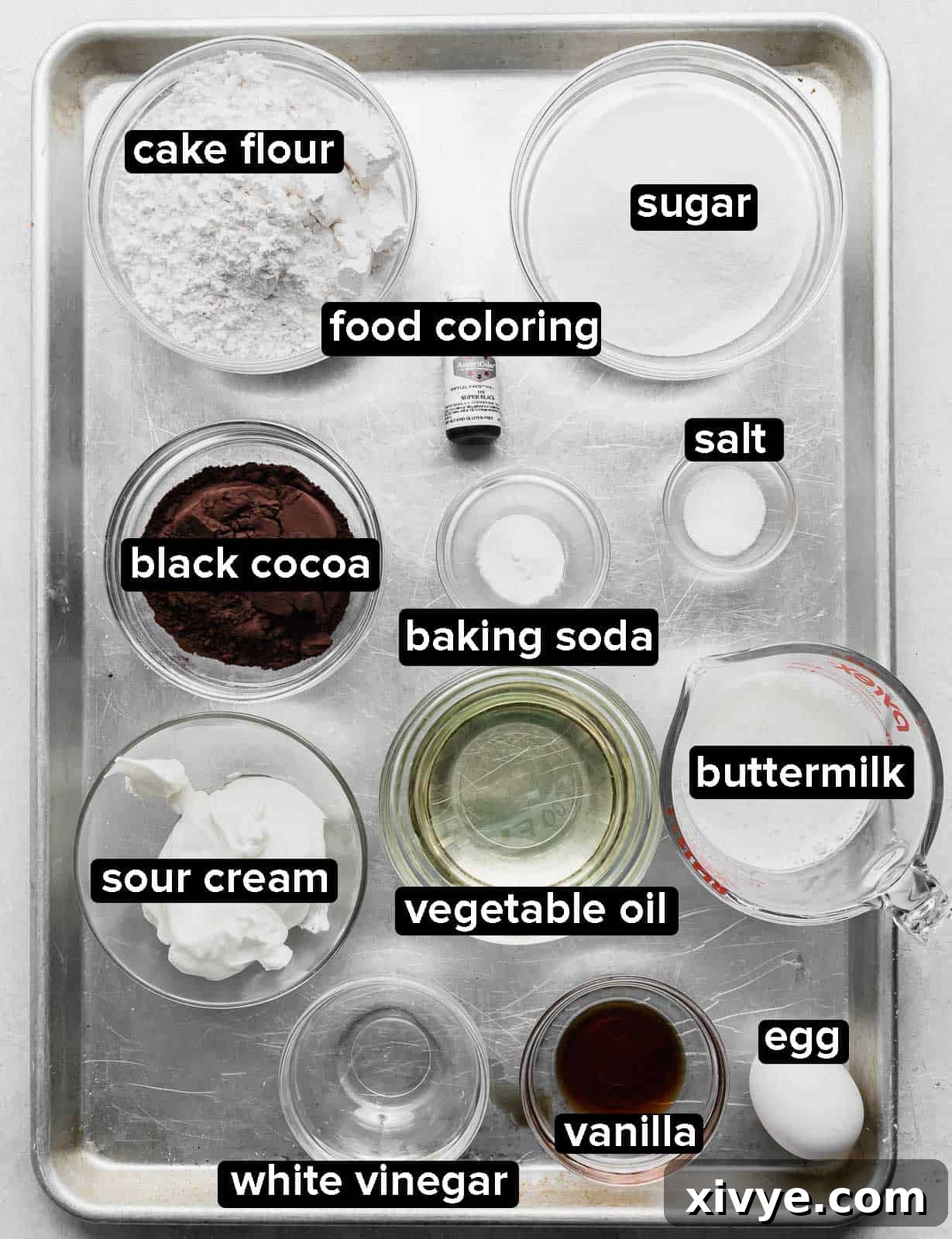 A collection of dry ingredients for Black Velvet Cupcakes, including flour, black cocoa powder, and sugar, artfully arranged on a baking sheet, ready for mixing.
