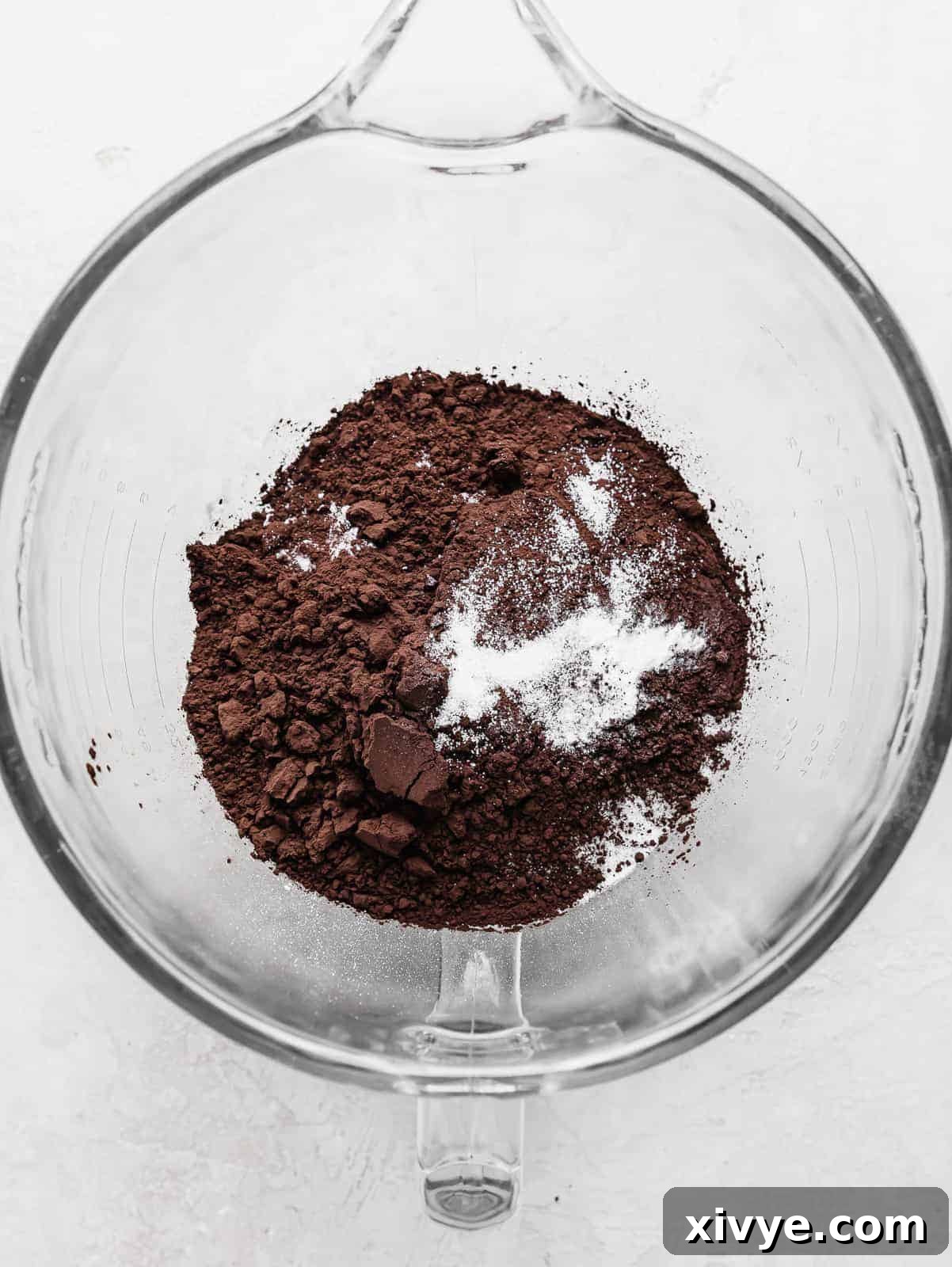 A clear glass mixing bowl filled with the dry ingredients for Black Velvet Cupcakes, including black cocoa powder, flour, salt, and baking soda, clearly visible before mixing.