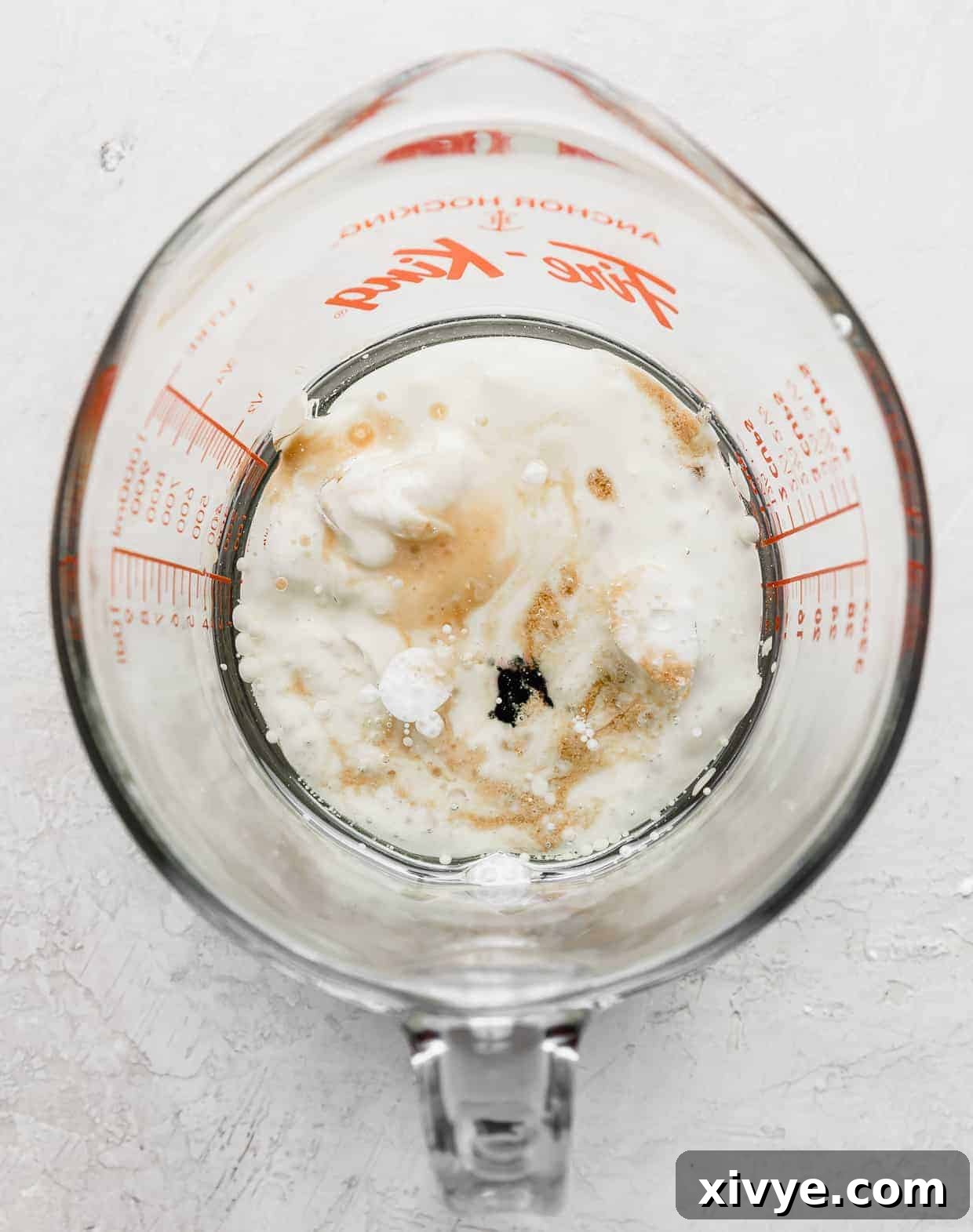 A glass measuring cup containing the wet ingredients for Black Velvet Cupcakes, including oil, sour cream, buttermilk, egg, vanilla extract, white vinegar, and black food coloring, before mixing.