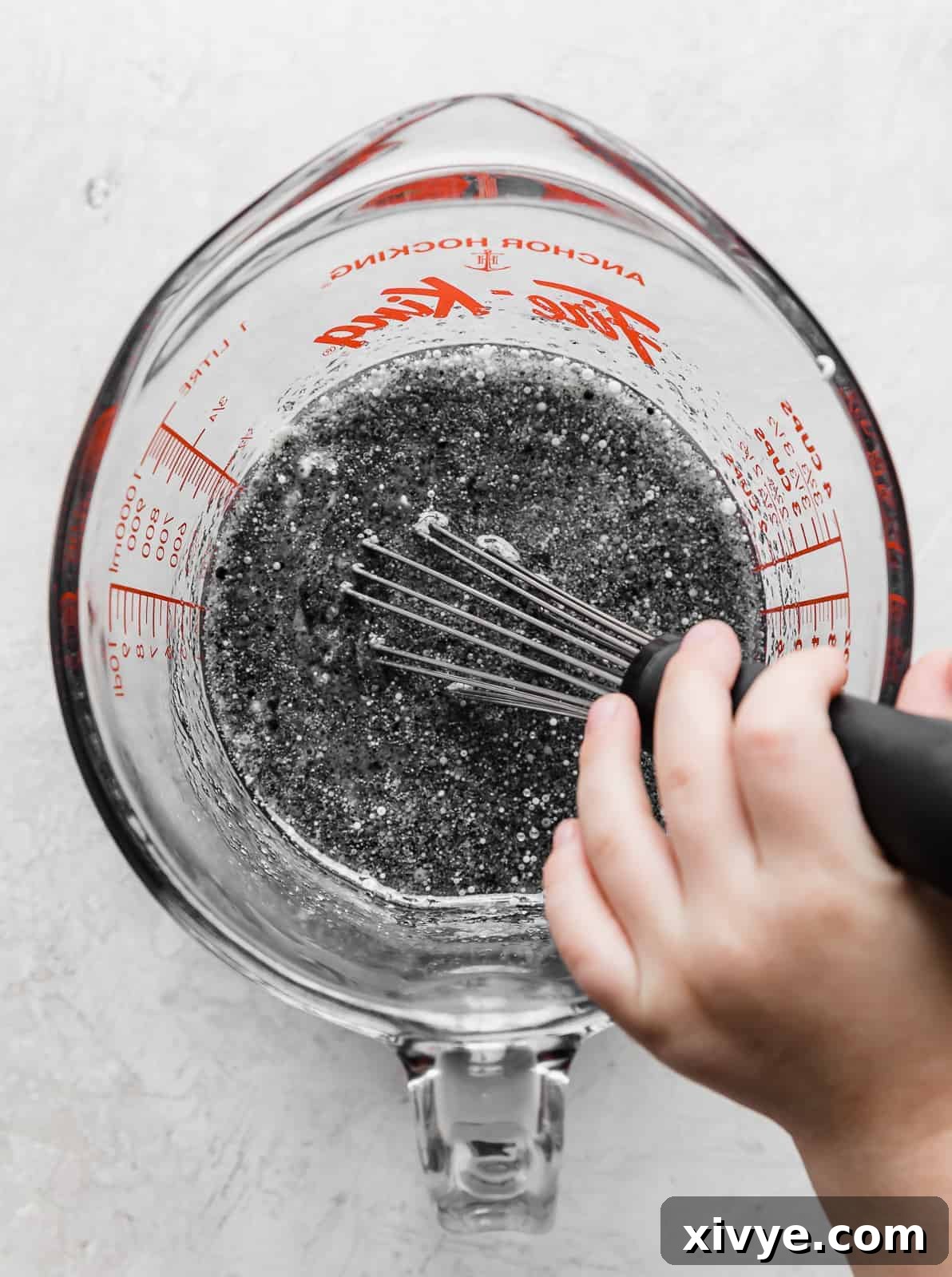 A dark gray liquid mixture, comprising the wet ingredients for Black Velvet Cupcakes, being whisked in a glass measuring cup to combine thoroughly and distribute the black food coloring.