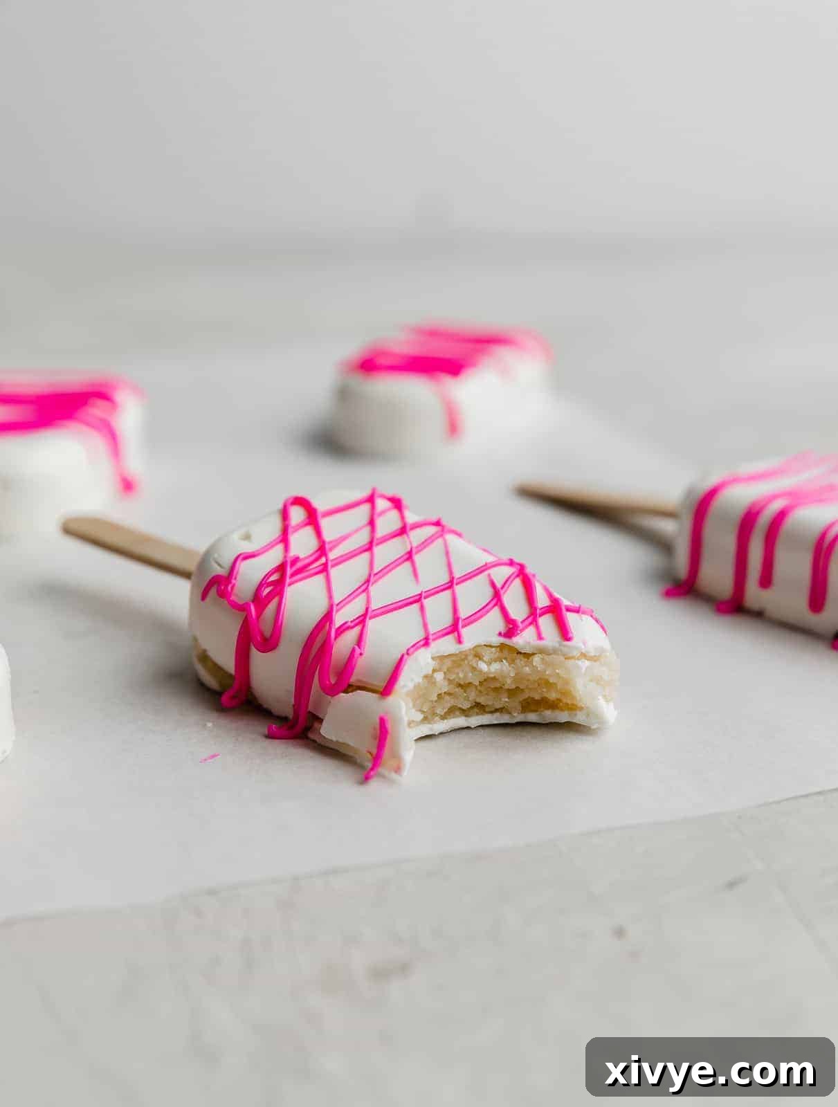 Delightful Cake Lollies 11 A pristine white covered Cakesicle, with a perfectly tempting bite taken out, resting on a clean white background.