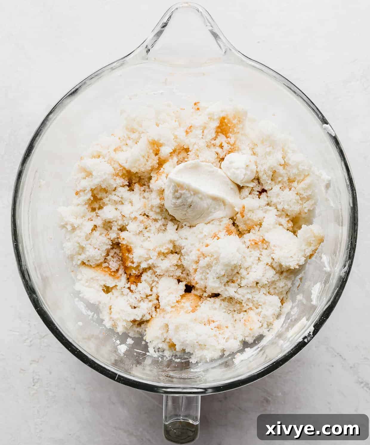Delightful Cake Lollies 5 A mix of crumbled white cake and a dollop of creamy frosting, elegantly presented in a clear glass mixing bowl.