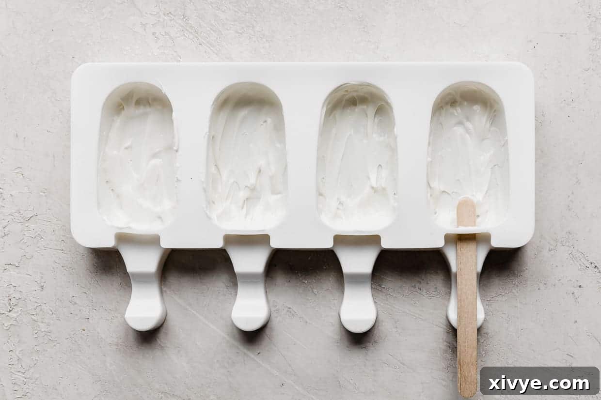 Delightful Cake Lollies 7 A pristine white cakesicle mold, partially filled with melted white chocolate, and a single popsicle stick resting beside it.
