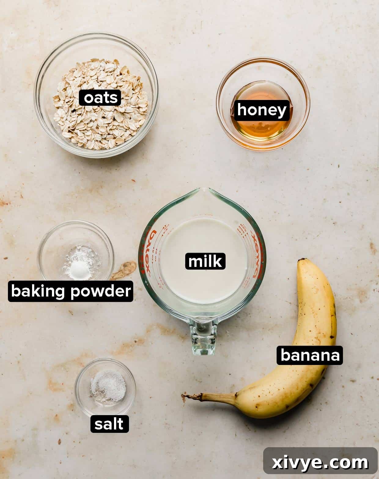 Ingredients used to make Baked Oats on a cream background, including oats, honey, banana, and milk.