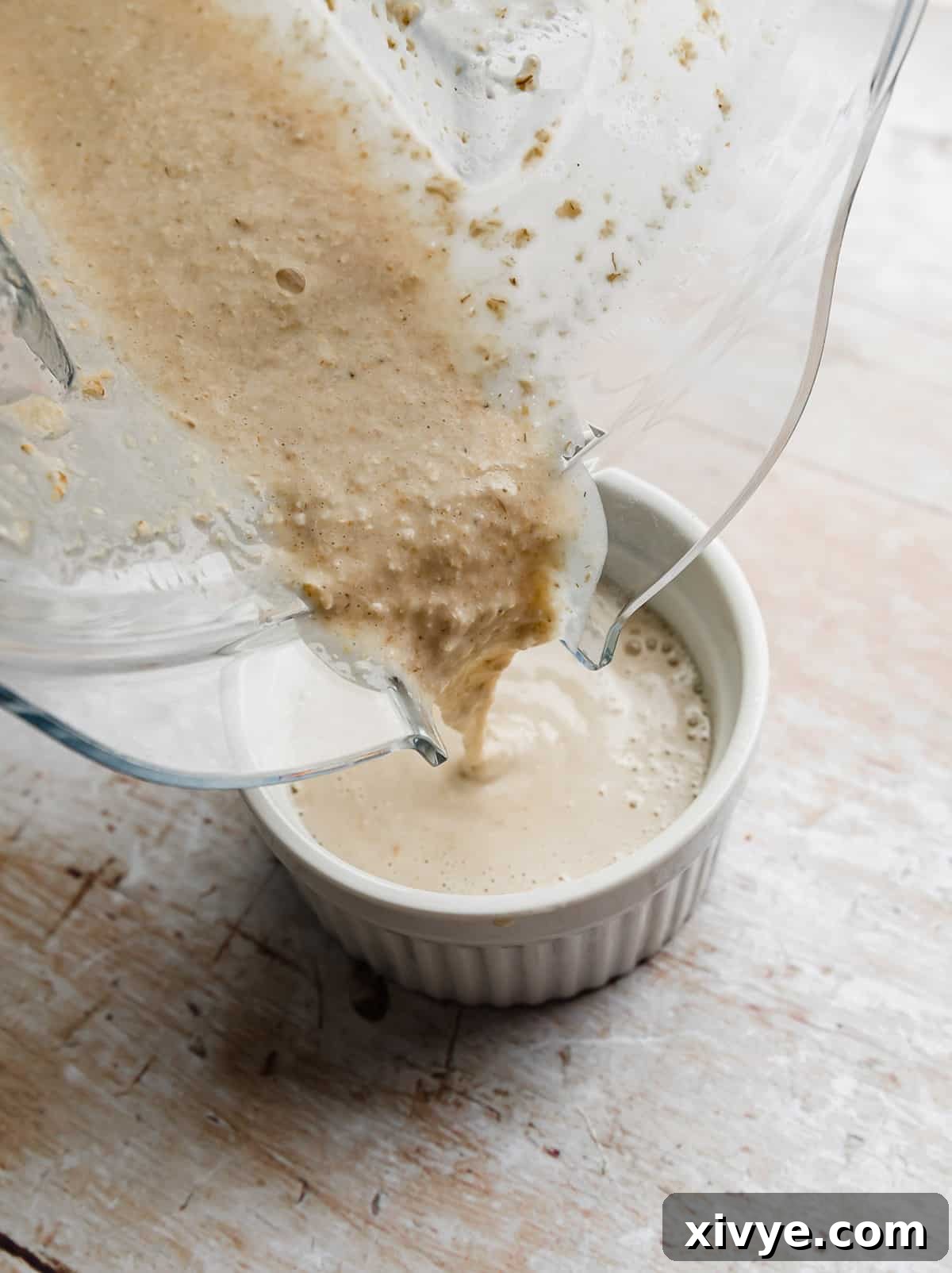 Baked oats mixture being poured into a white ramekin from a blender.