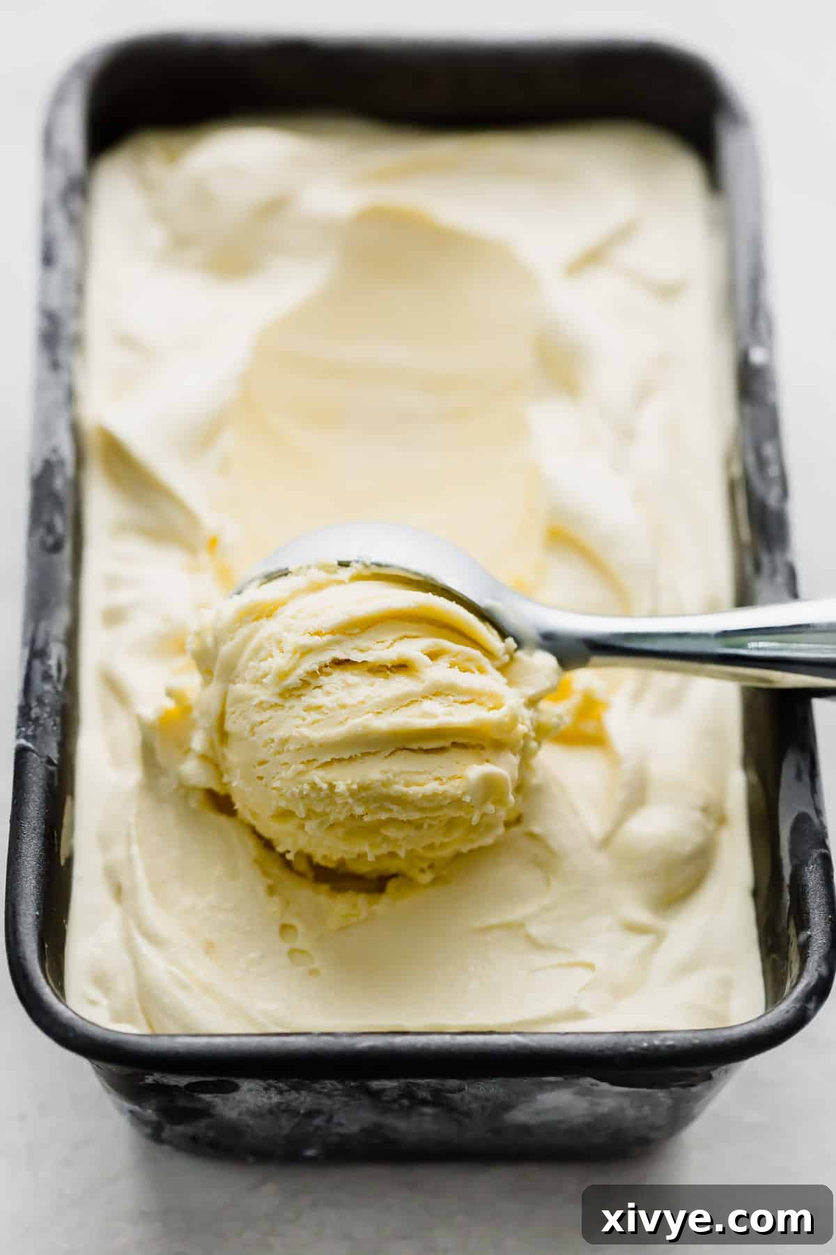 Homemade Vanilla Ice Cream in a bread pan with an ice cream scooping spooning out a portion.