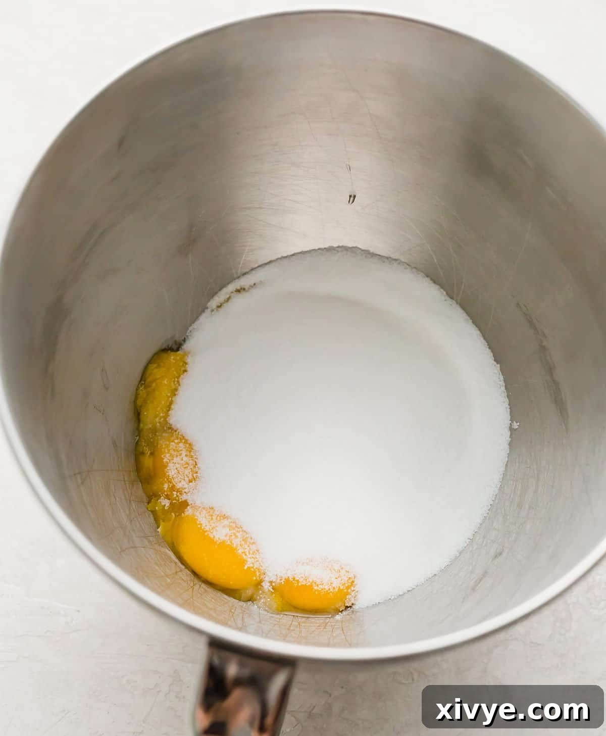 Sugar and egg yolks in a metal mixing bowl.