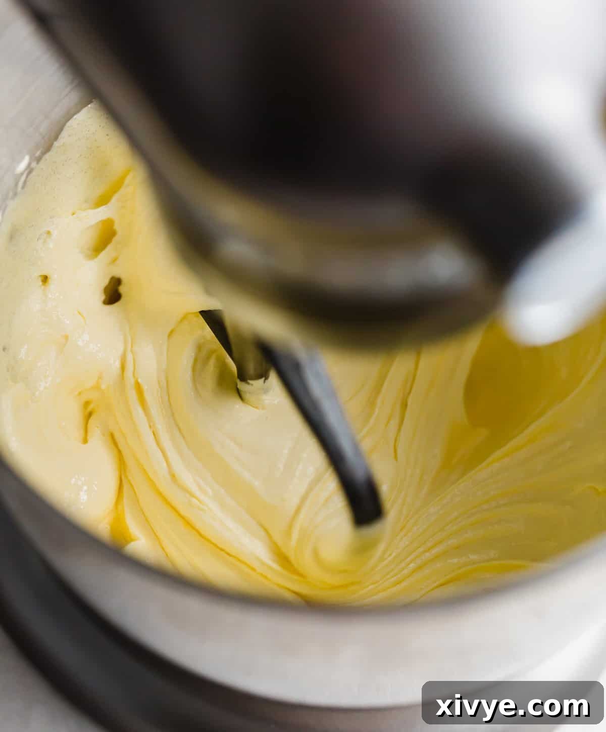 A light yellow fluffy mixture being mixed by a stand mixer.