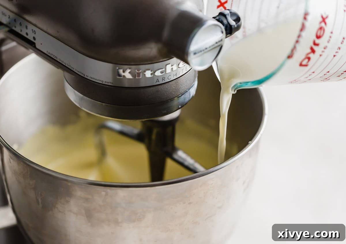 A white hot liquid being poured into a Homemade Vanilla Ice Cream custard mixture in a stand mixer.
