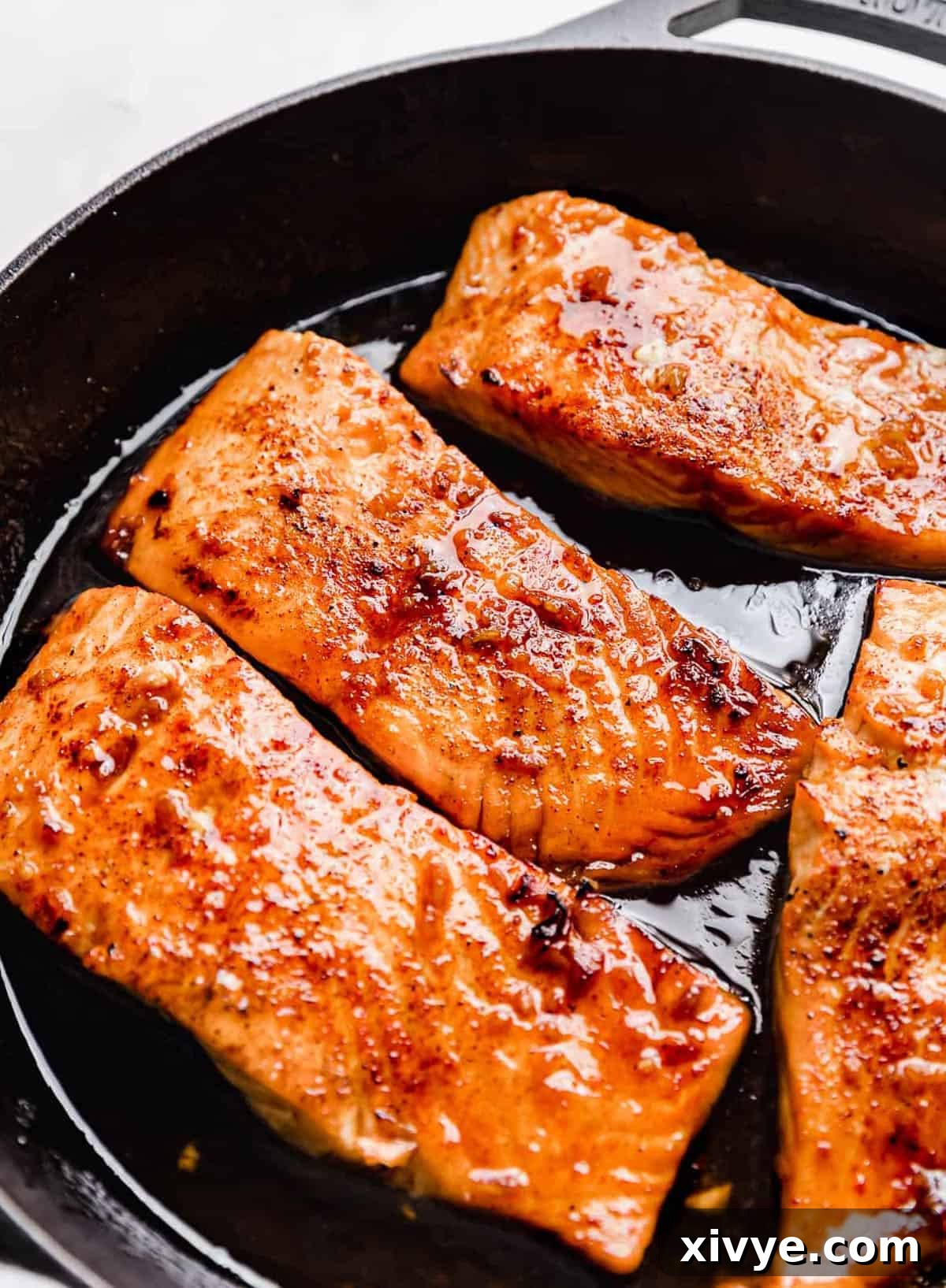 Sticky Honey Garlic Salmon 2 Honey Garlic Baked Salmon in a black cast iron skillet, garnished with fresh herbs.