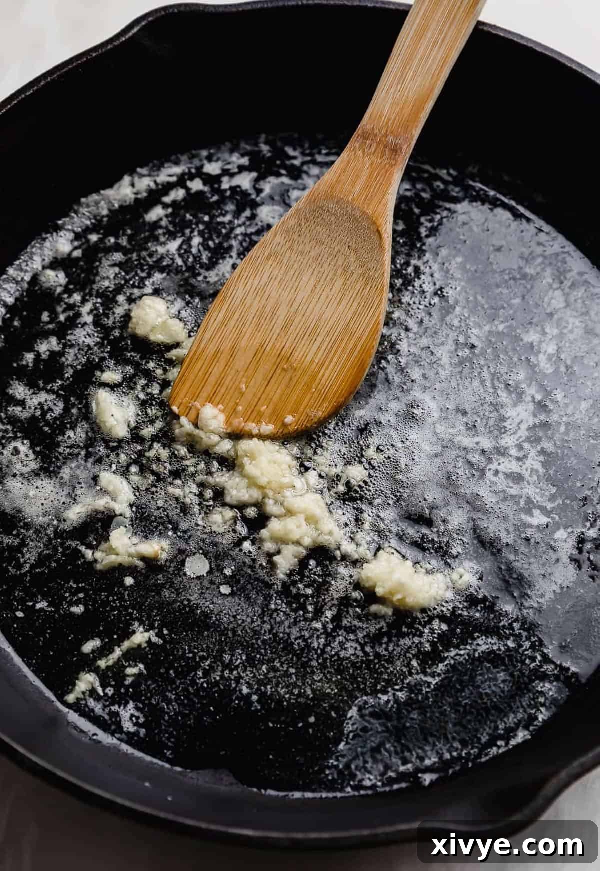 Sticky Honey Garlic Salmon 4 A wooden spoon stirring minced garlic in a cast iron skillet, starting the sauce.