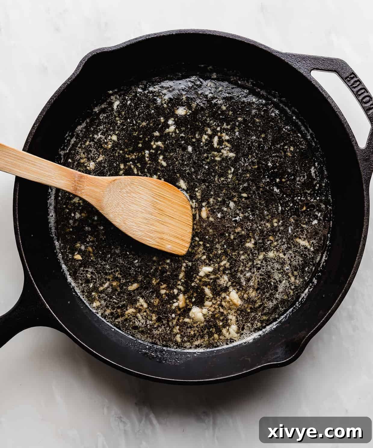 Sticky Honey Garlic Salmon 5 An overhead photo of a light colored honey garlic sauce simmering in a black skillet.